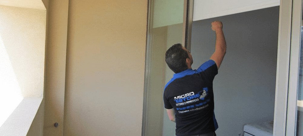 Técnico da MicroEstore, de camisola com o logótipo da empresa, a instalar um estore numa janela