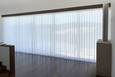 Cortina de voile branco em calha de madeira escura numa sala ampla com pavimento de madeira