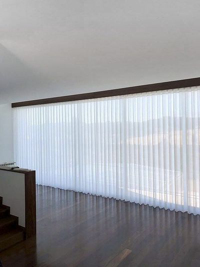 Cortina de voile branco translúcido em calha de madeira escura junto a escadas de madeira