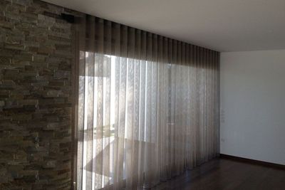 Cortina translúcida cinzenta junto a parede de pedra e envidraçado numa sala ampla