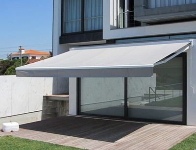 Toldo extensível branco sobre deck de madeira junto a moradia moderna com parede de mármore
