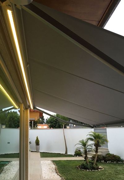 Vista inferior de toldo bege com fita LED sobre pátio ajardinado com palmeiras