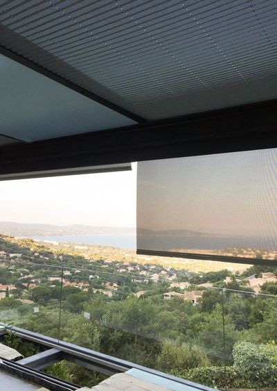 Estore exterior de rolo parcialmente descido sob pérgola, com vista panorâmica para a baía
