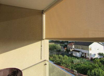 Estores exteriores de rolo bege em varanda com vista para casas e horta ao entardecer