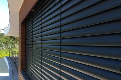 Estore exterior de lâminas pretas em perspetiva sobre uma fachada revestida a madeira