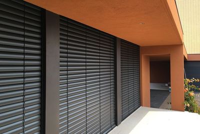 Estores exteriores de lâminas pretas em fachada de moradia terracota com pilar e entrada