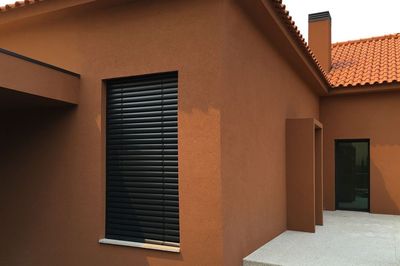 Estore exterior de lâminas pretas fechado numa janela de moradia terracota com telhado de telha