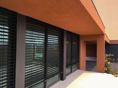 Estores exteriores de lâminas pretas orientáveis em janelas de moradia terracota com pilar