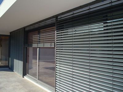 Estores exteriores de lâminas metálicas em fachada envidraçada de moradia moderna sob sol forte