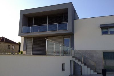 Moradia moderna de dois pisos com estores exteriores de lâminas escuras e escada com guarda de vidro