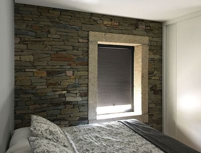 Estore de rolo escuro numa janela com moldura de granito e parede de pedra num quarto
