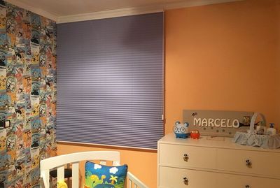 Estore plissado azul num quarto de criança com papel de parede ilustrado e cómoda