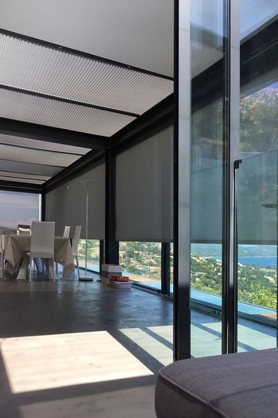 Estores de rolo screen e estore de teto plissado numa sala envidraçada com vista para o mar