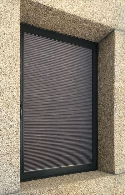 Estore interior tipo favo de mel castanho numa janela de moldura de granito, visto do exterior