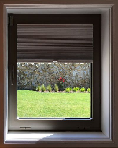 Estore interior tipo favo de mel meio descido numa janela com vista para relvado e muro de pedra