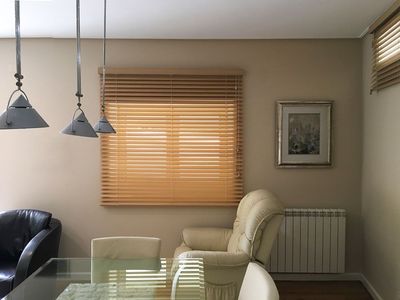 Estore de lâminas de madeira cor de mel numa sala de jantar com candeeiros suspensos