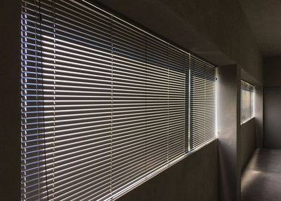 Estore de lâminas metálicas numa longa janela de corredor em betão com luz lateral marcada