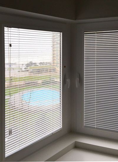 Estores de lâminas brancas em janelas de canto com vista para relvado e piscina exterior