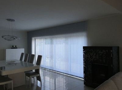 Cortina de lâminas verticais cinzentas numa porta envidraçada de sala de jantar com lareira