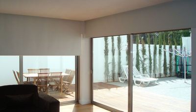 Estore de rolo bege numa ampla porta de correr envidraçada com vista para terraço e jardim
